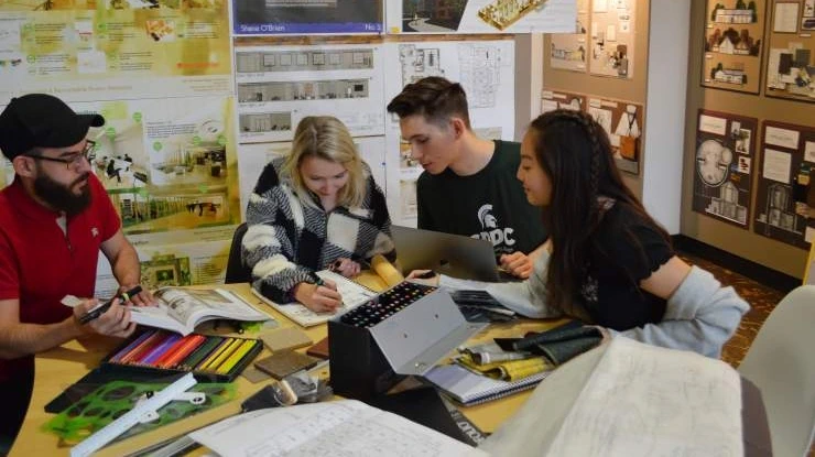 Students working toward an interior design degree sit at a table surrounded by colorful interior design materials.